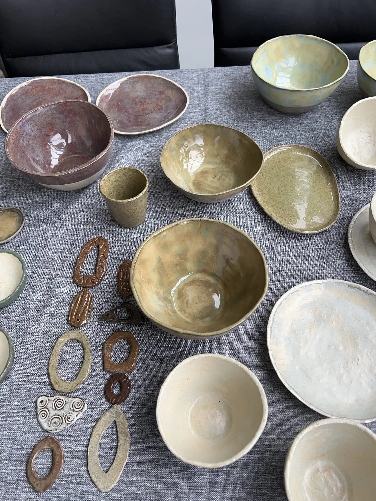 Werktisch im Atelier mit Keramikschalen und -tellern in Erdtönen sowie kleinen Keramik-Anhängern.