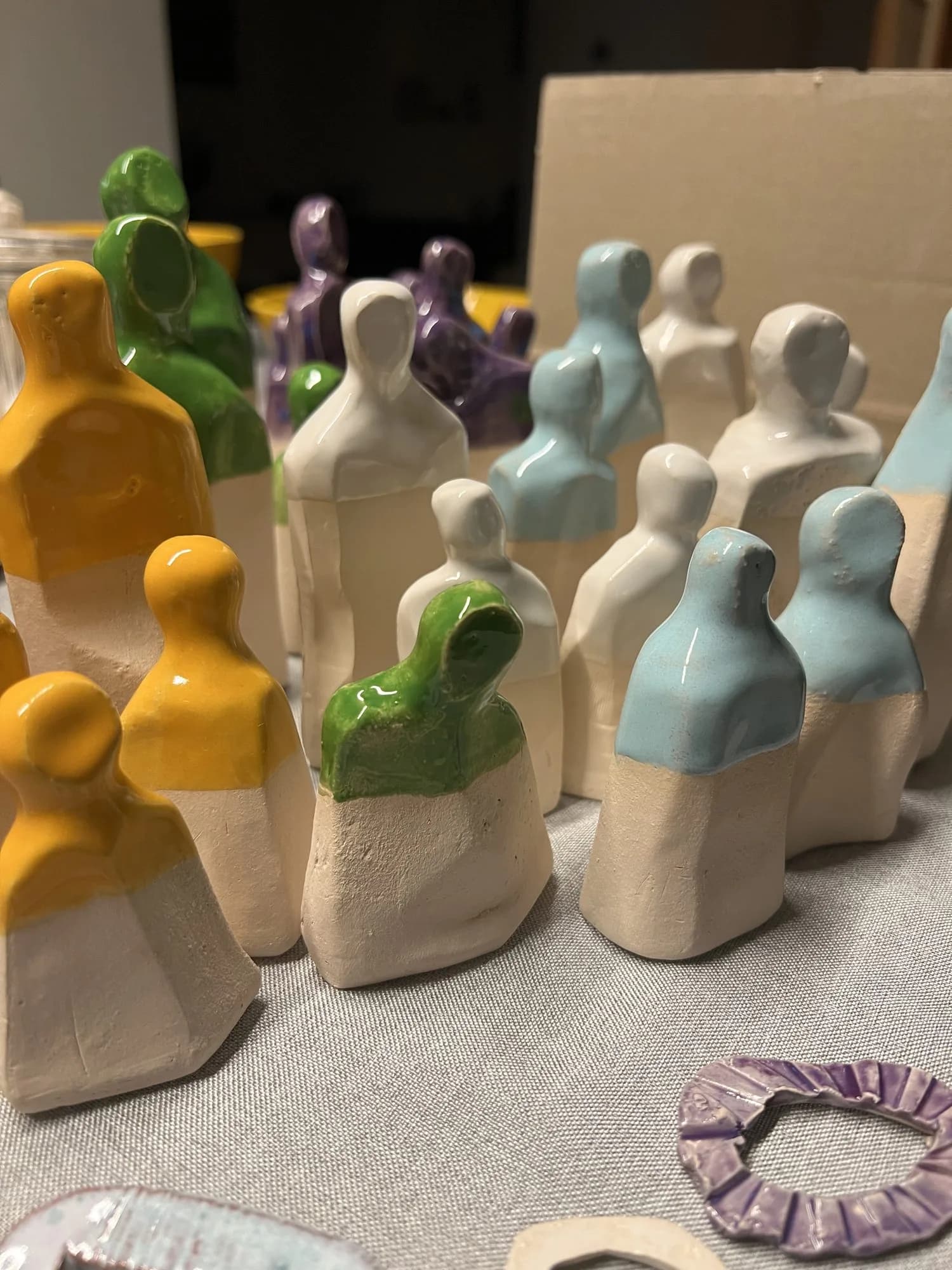 Kleine glasierte Keramikfiguren in Gelb, Grün, Weiß und Violett, wie eine Figurengruppe aufgestellt.