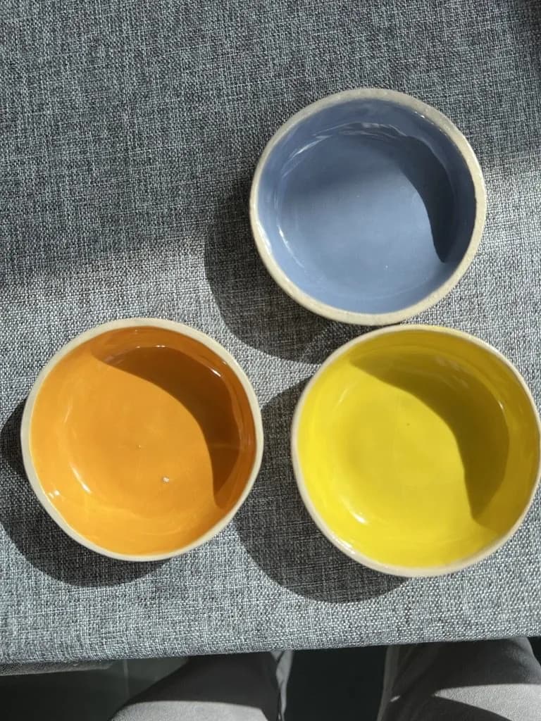 Drei kleine Keramikschälchen in Graublau, Orange und Gelb von oben fotografiert.