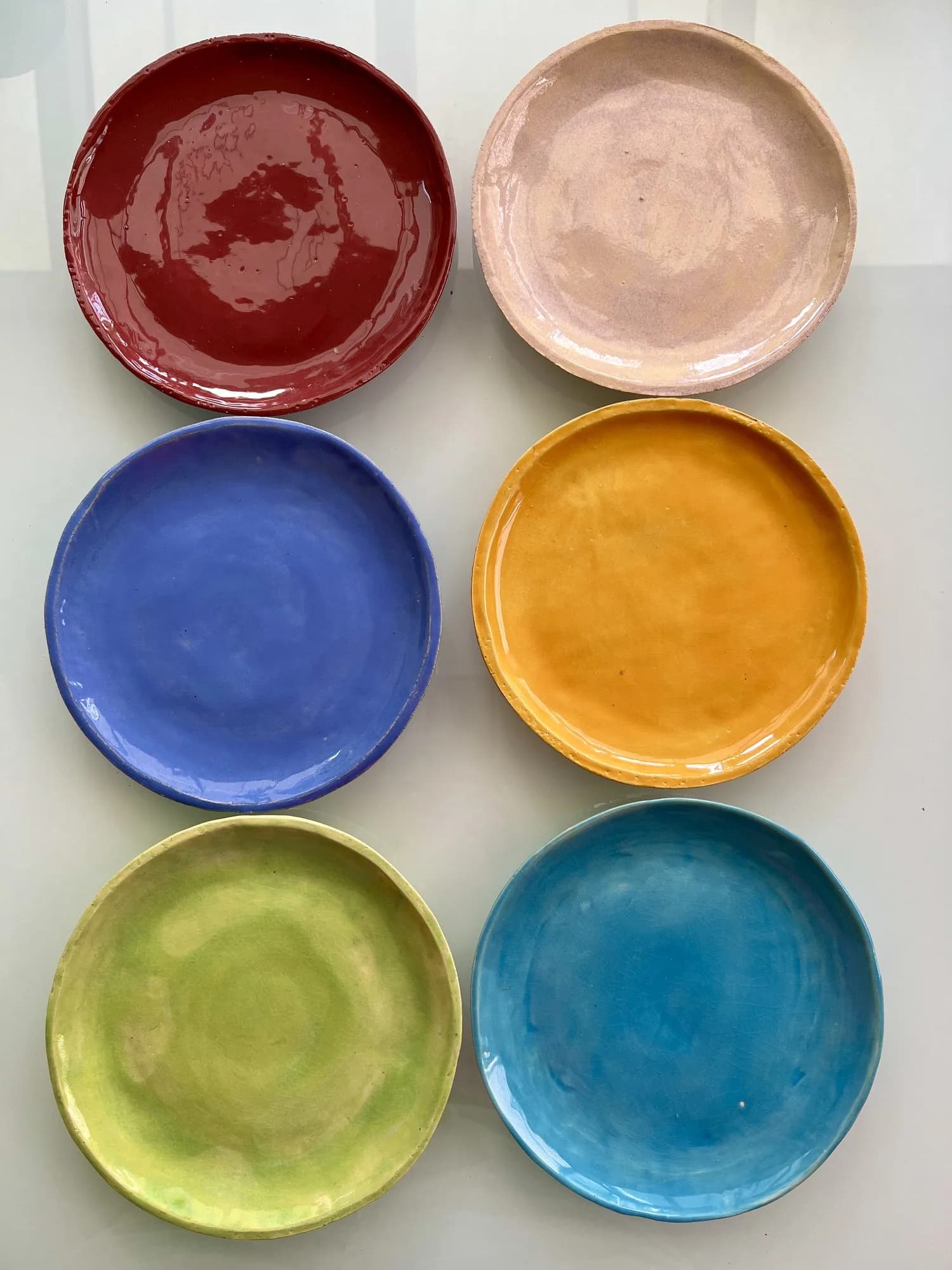 Sechs Keramikteller im Raster in Dunkelrot, Beige, Blau, Gelb, Grün und Türkis.