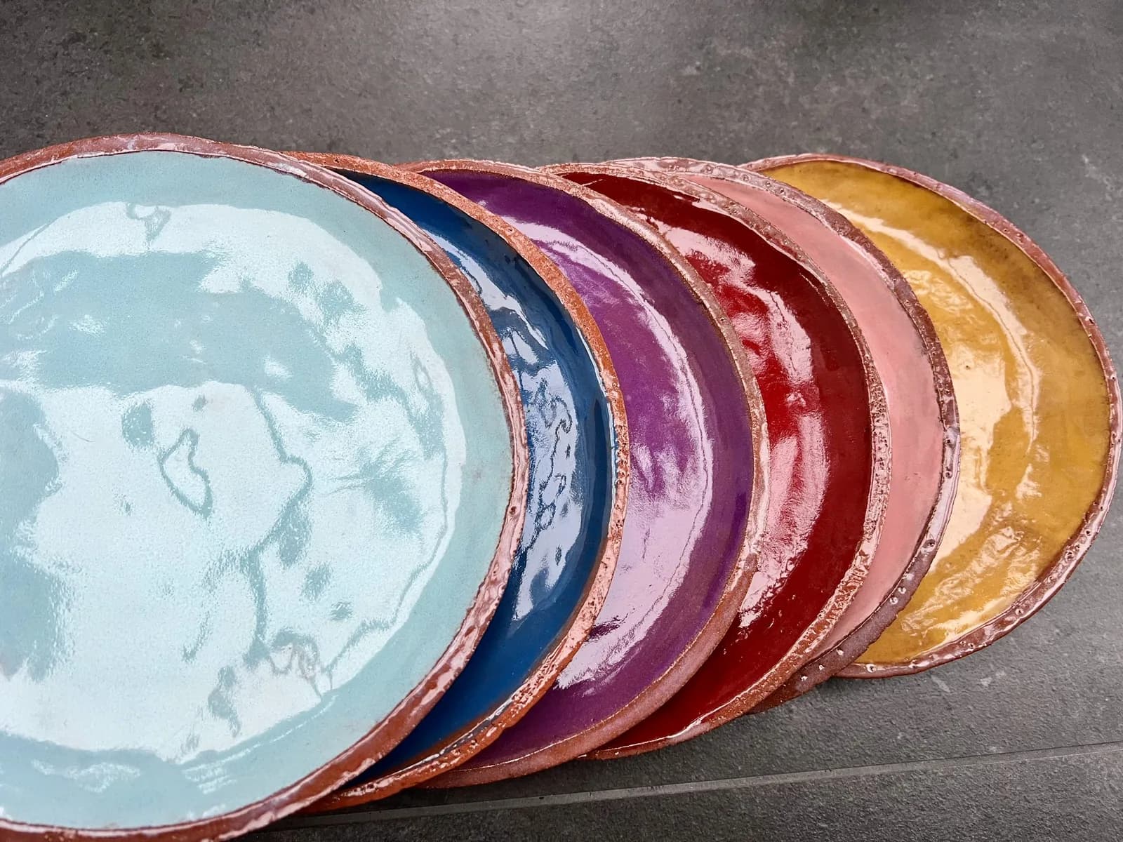 Fächerartig aufgestellte Keramikteller in Hellblau, Blau, Violett, Rot, Rosa und Gelb.